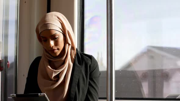 Front view of young Asian woman in hijab using digital tablet and travelling in train 4k