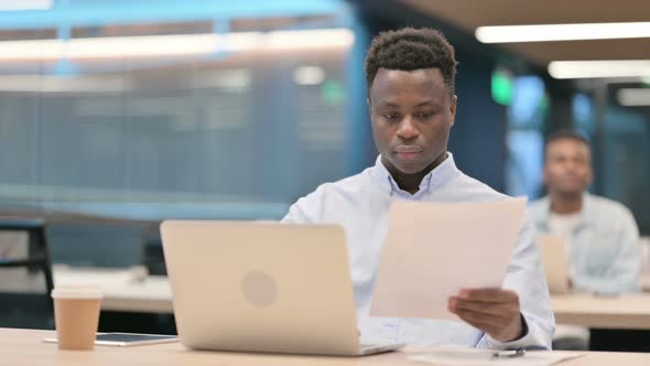 Businessman with Laptop Reading Documents in Office