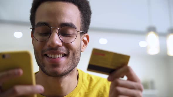 A Happy Young Man Making a Purchase at an Online Store Using a Card and a Smartphone