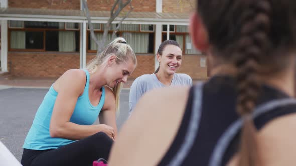 Diverse female basketball team sitting on ground and talking