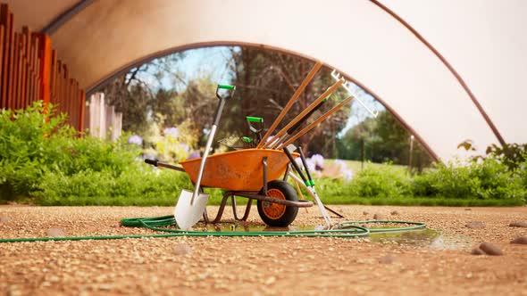 Garden tools gathered around a wheelbarrow in a beautiful, lush garden. 4KHD