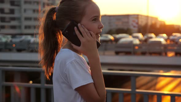 Schoolgirl Talks on Smartphone with Concentration at Sunset