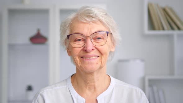 Aged lady with short grey hair and glasses looks straight