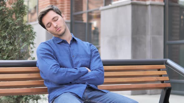 Young Man Sleeping while Sitting Outdoor on Bench