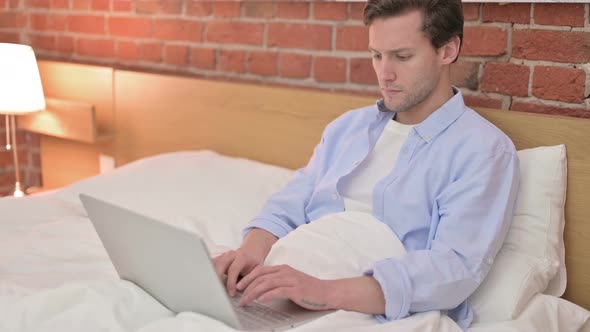 Focused Young Man Using Laptop in Bed