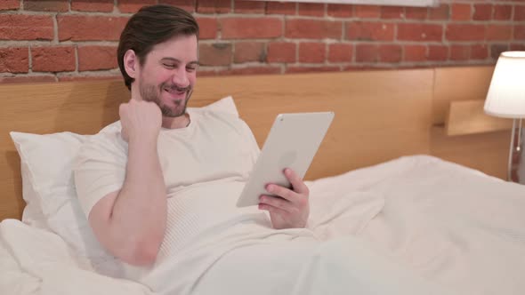 Casual Young Man Celebrating Success on Tablet in Bed