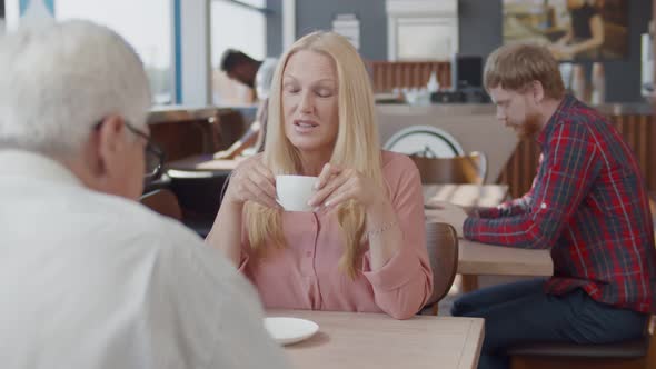 Mature Couple Sitting at Table and Drinking Coffee in Modern Cafe