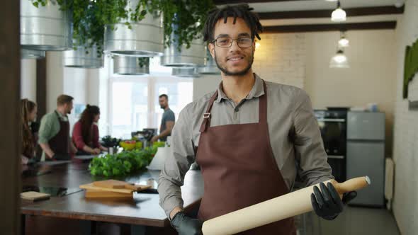 Portrait of Cheerful Afro-American Guy in Apron Holding Rolling Pin in Cookery Class