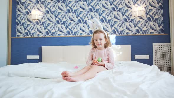 A Cute Little Girl is Sitting on the King Size Bed with Her Legs Stretched Forward