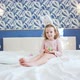 A Cute Little Girl is Sitting on the King Size Bed with Her Legs Stretched Forward - VideoHive Item for Sale