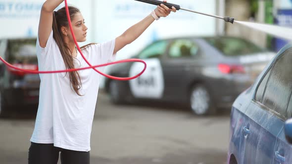 Young Woman Washing Blue Car at Car Wash