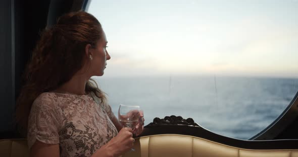 Woman Watching Sunset From Window On Luxury Cruise Ship with a Glass of Wine