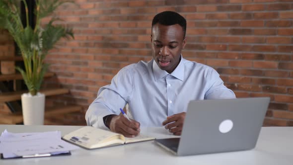 Focused African American Businessman Writing Notes in Notebook During Online Webinar is Improving