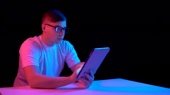 Young Man with a Tablet. A Man Is Using a Tablet. Blue and Red Light Falls on a Man on a Black