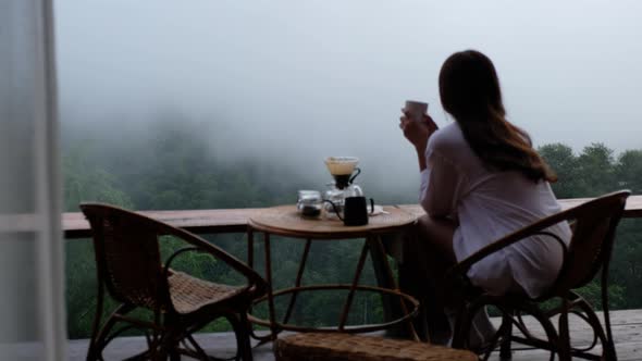 Blurred of a woman drinking drip coffee and looking at a beautiful nature view on foggy day