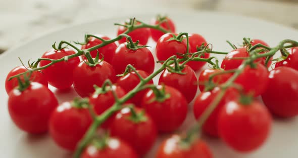 Video of fresh cherry tomatoes on white plate over wooden background