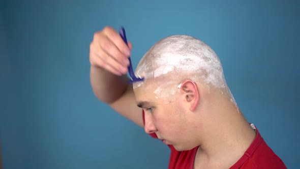 The Bald Young Man Insolently Shaves His Head. A Man Cuts His Hair with a Razor on a Blue Background