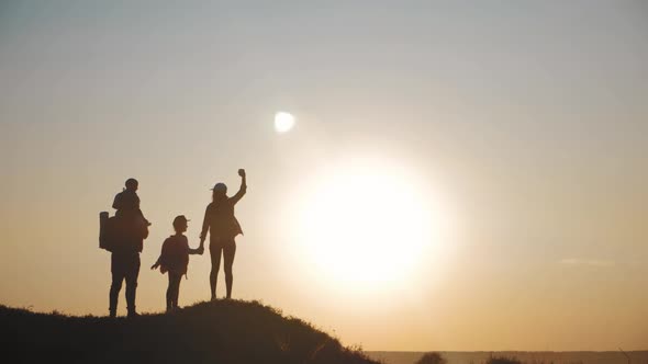 Silhouettes of Father, Mother and Children Hiking. Baby Sits on the Shoulders of His Father. Hiking