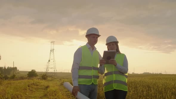 Engineers in Uniform Working with a Laptop Near Transmission Lines