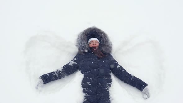 Happy Girl Lying on a Snow and Shows Angel