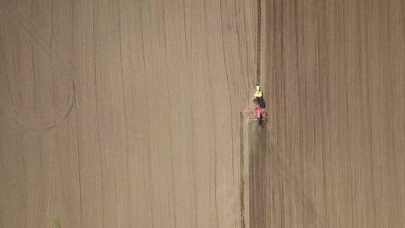 Top down aerial view of green tractor cultivating ground and seeding a dry field. Farmer preparing 