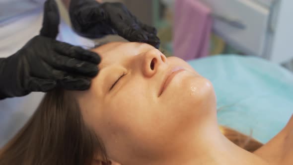 Cosmetologist Applies Nourishing Cream to Fair Skin of Woman's Face in Circular Movements