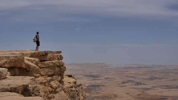 Man with Backpack Standing on the Desert Mountain Rock Cliff Edge