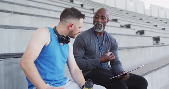 Diverse male coach and athlete talking during night training session