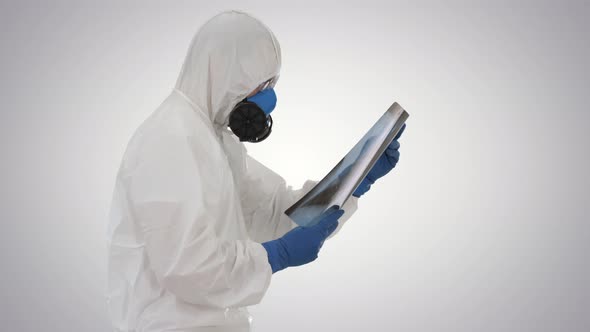 Doctor in Protective Suit Looking at Lungs X-ray While Walking on Gradient Background