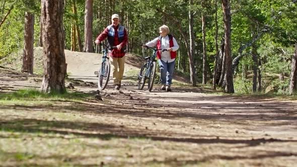 Active Pensioners Walking with Bicycles in Forest