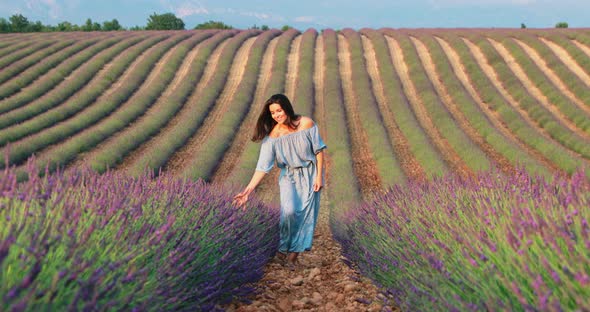 The Beautiful Young Girl Walks Across the Field of a Lavender at Sunset She is Wearing a Long Blue