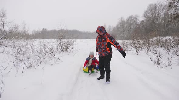 Happy Dad Sledges a Child on a Snowy Road. Christmas Holidays. Father Plays with His Daughter