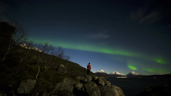 Snow-Capped Mountains and Man Standing By the Rocks in Lake Admiring Northern Lights