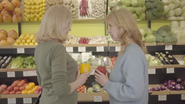 Two Adult Women with Red and Yellow Bell Peppers Talking, To Camera and Smiling. Portrait of
