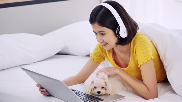 Young woman using laptop in bed with her Maltese dog.