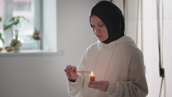 A Young Woman in Hijab Ignites Incense From the Candle Then Looks in the Camera