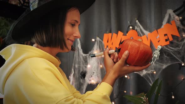 Halloween celebrating. Woman painting spooky face on orange pumpkin