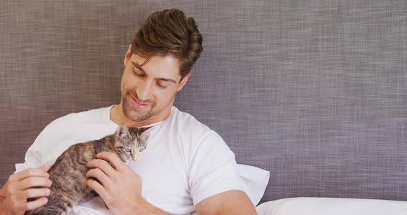 Young man sitting on bed stroking his tabby cat 4K 4k