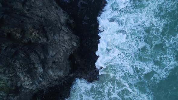 Aerial of waves crashing against UK coast, top down view