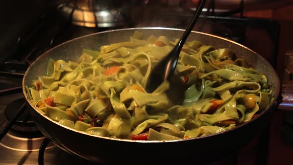 Mixing homemade egg noodles with vegetables on hot pan with plastic spoon.