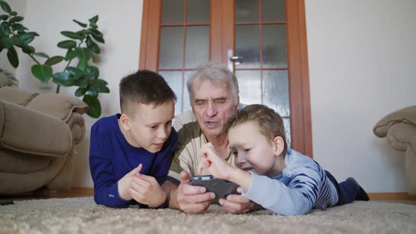 Two grandchildren are teaching grandfather to play their favorite toy on the tablet