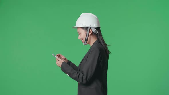 Side View Of Smiling Asian Female Engineer Using Smartphone And Walking In The Green Screen Studio