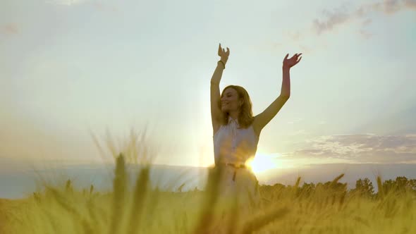 Happy Girl Raising Hands in Wheat Field at Sunset