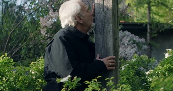 Sad Old Gray Haired Man Stands Near Big Old Wooden Cross at the Cemetery