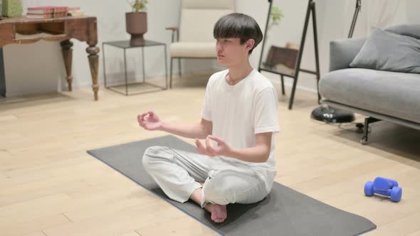 Peaceful Young Asian Man Meditating on Yoga Mat at Home
