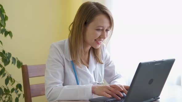 A nurse in a bathrobe and with a stethoscope works at a laptop