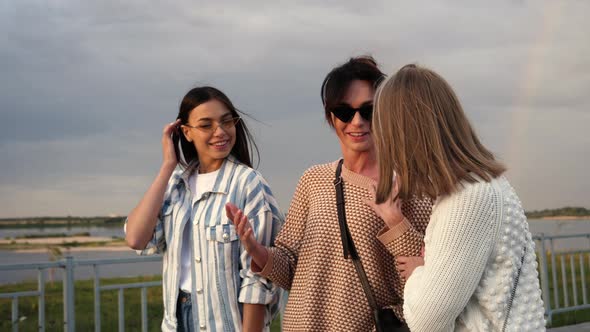 Three Young Women in Sunglasses Walk Along the Waterfront and Gossip.