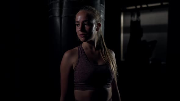 Medium Shot Portrait of Satisfied Confident Sportswoman Standing at Punching Bag Smiling Looking