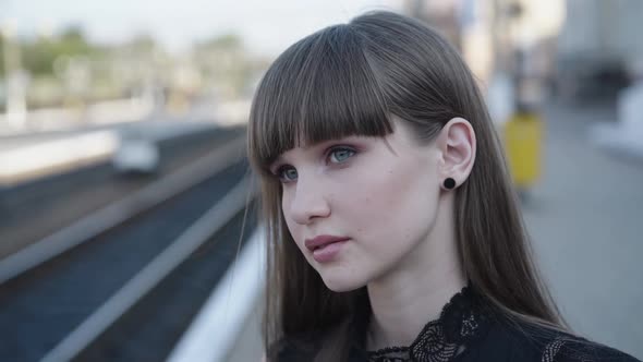 Portrait of Attractive Girl Looks Around on Railway Station and Smiles