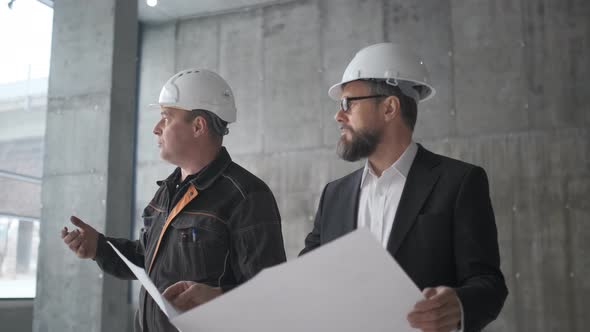 Two Man Engineers Have Conversation And Looking At Large Blueprint